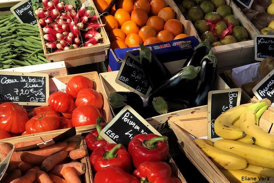 Imagen: puesto de mercado. Hay cajas con rábanos, judías verdes, mandarinas, tomates, pimientos, zanahorias, plátanos, berenjenas...